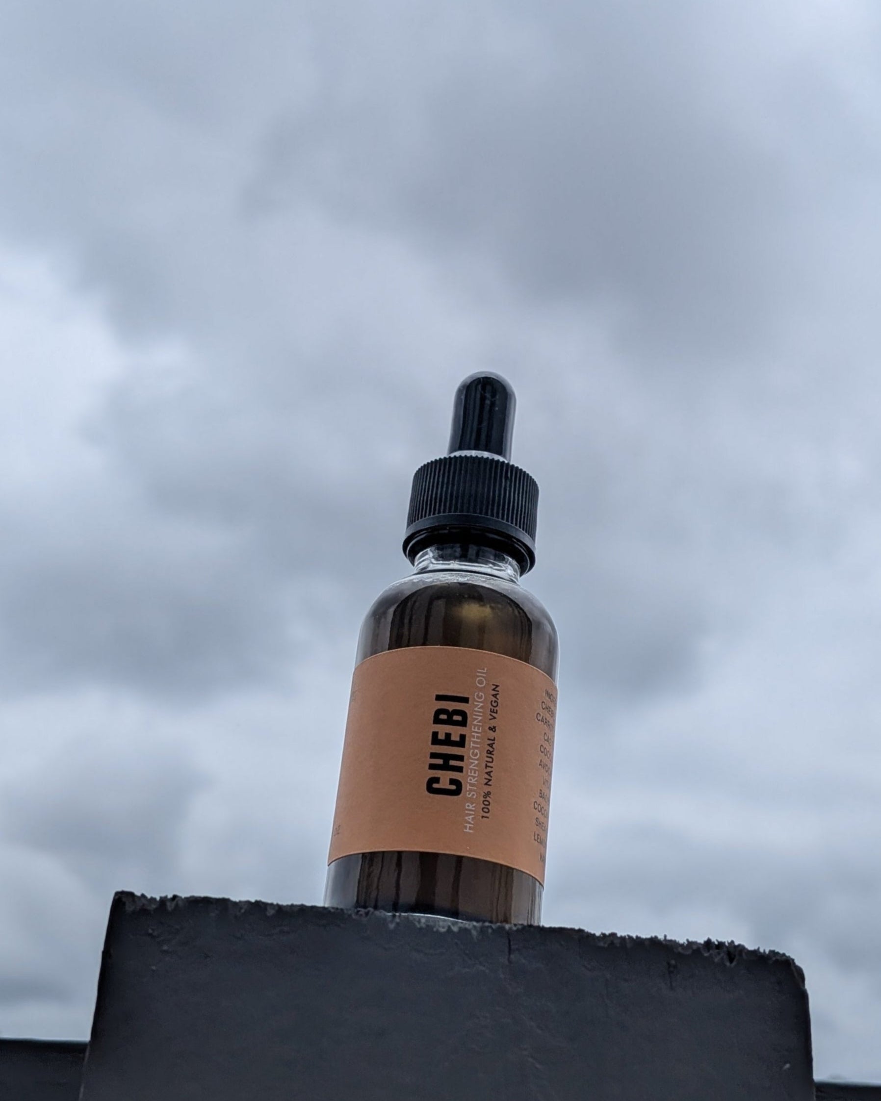Bottle with a dropper labeled 'Chebi Oil' against a cloudy sky