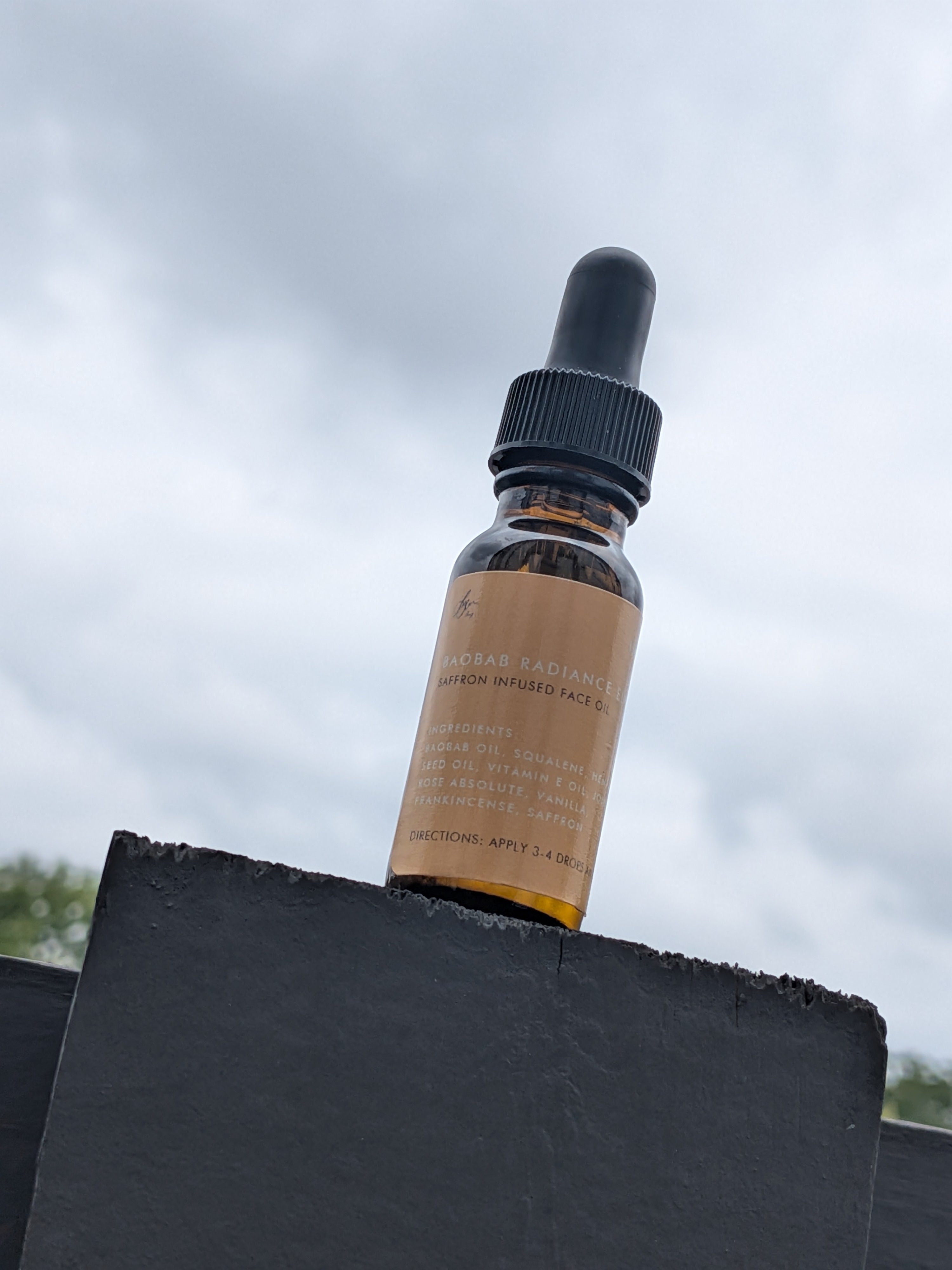 Bottle of skincare serum with a dropper on a black surface against a cloudy sky.