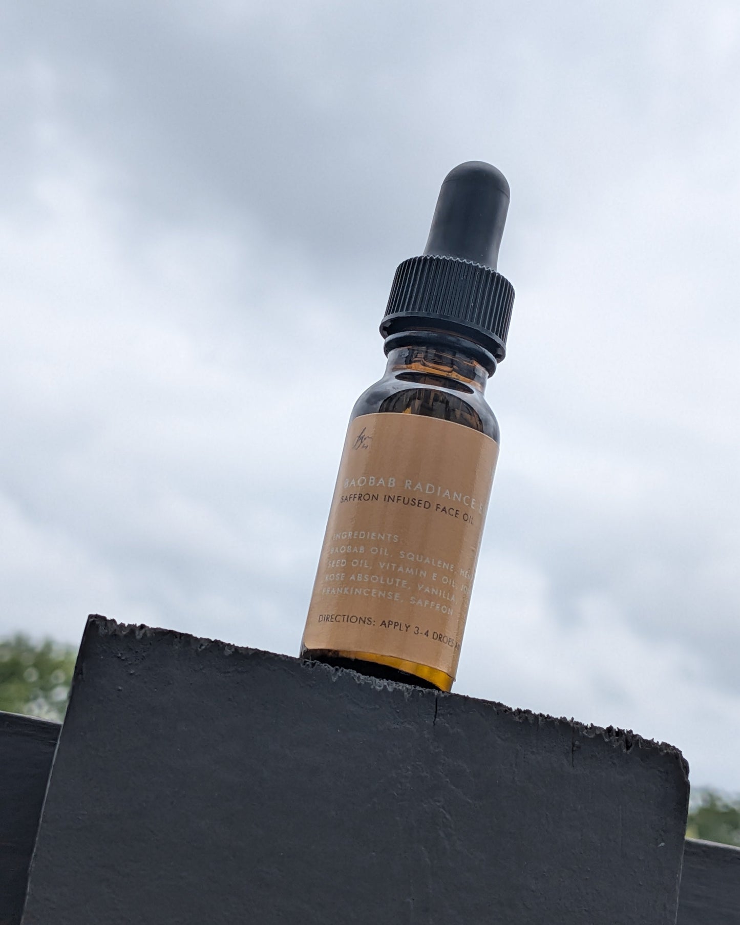 Bottle of skincare serum with a dropper on a black surface against a cloudy sky.